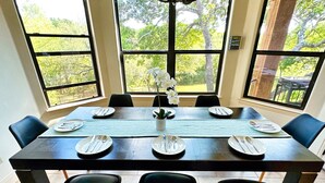 Een eettafel voor vier personen, compleet met stoelen, grote ramen en uitzicht op bomen.