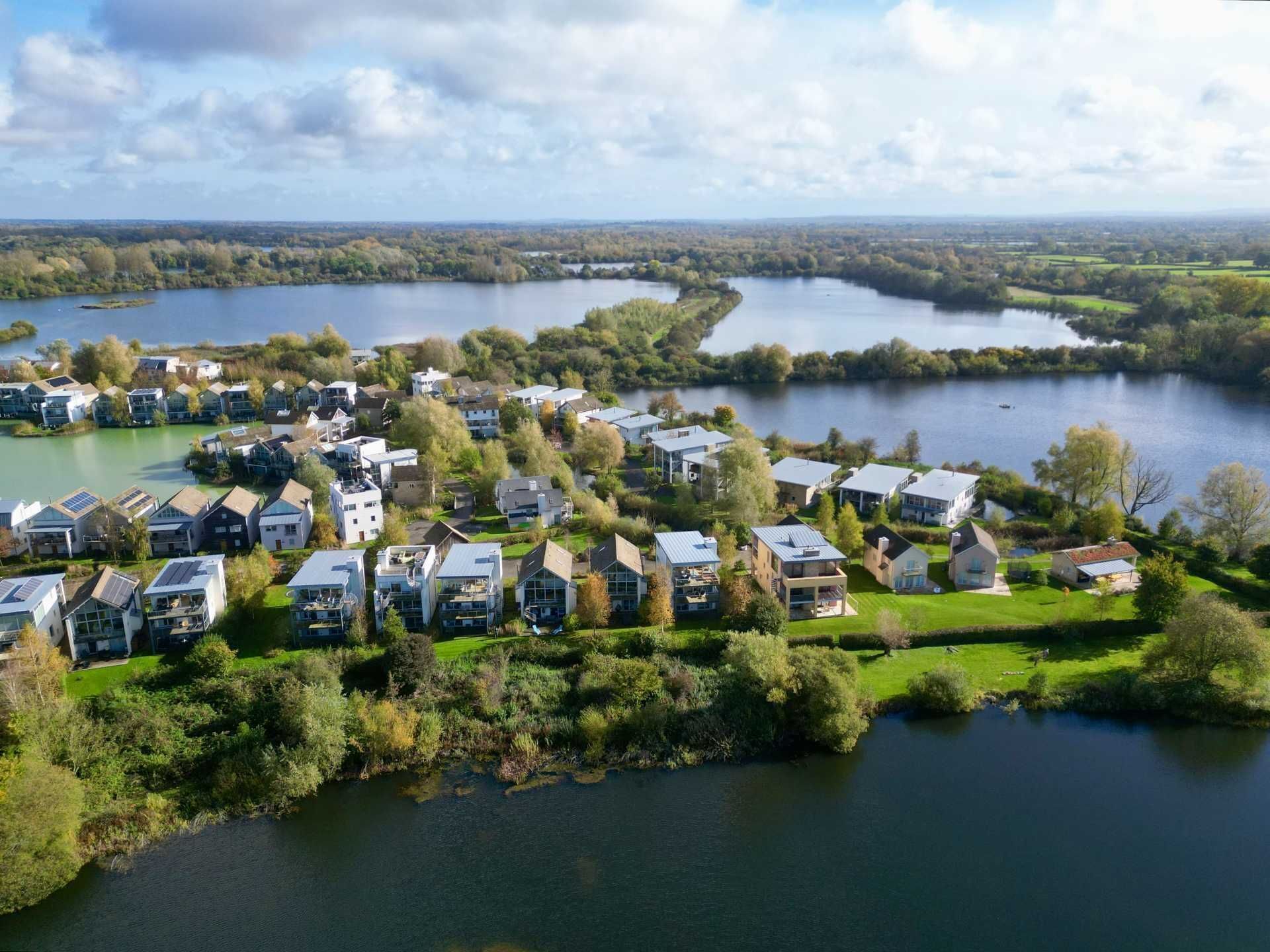 A residential area with houses along a river, surrounded by greenery and trees.