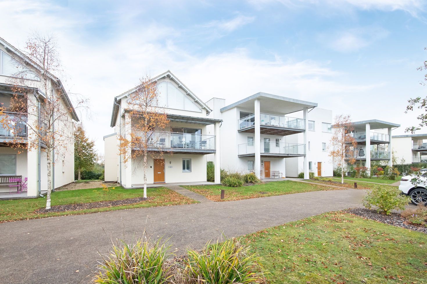 A modern residential building with multiple balconies, a paved driveway, and a well-maintained lawn.