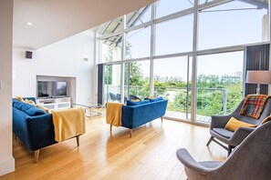 Un salón espacioso con un gran ventanal, televisión y muebles modernos.