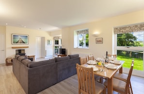 A modern living room with a grey sectional sofa, a dining table set for four, and a TV in the background.