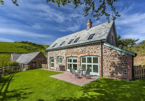 A stone house with a patio, a dining area, and a view of the surrounding landscape.