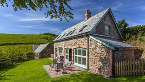 A stone house with a sloped roof, a patio with outdoor furniture, and a wooden fence. - Dashel Cottage, Countisbury (Lynmouth)