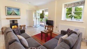 A living room with a fireplace, sofa, television, and a view of the outdoors. - Dashel Cottage, Countisbury (Lynmouth)