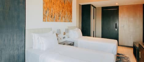 A hotel room with two beds, a large abstract painting on the wall, a modern door, and a small table with a lamp.