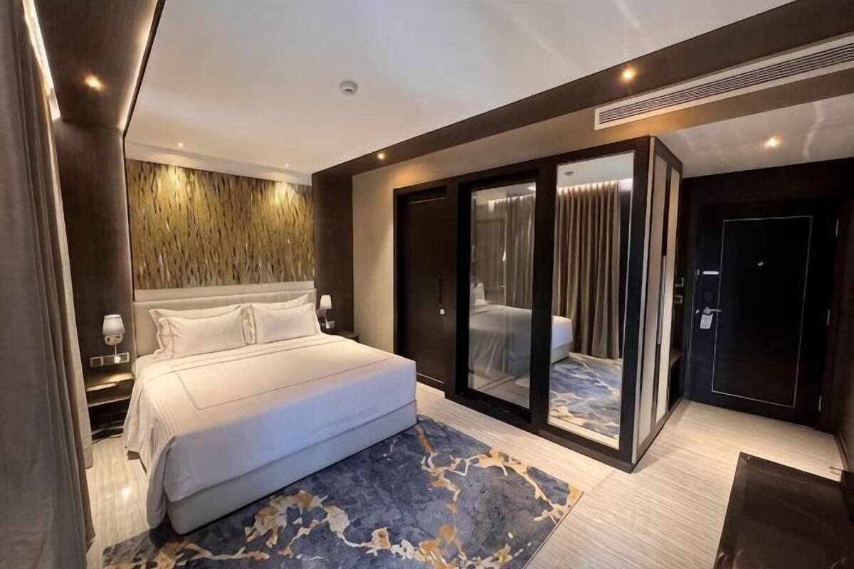 A modern bedroom with a large bed, a glass door leading to a balcony, and a marble-patterned rug.