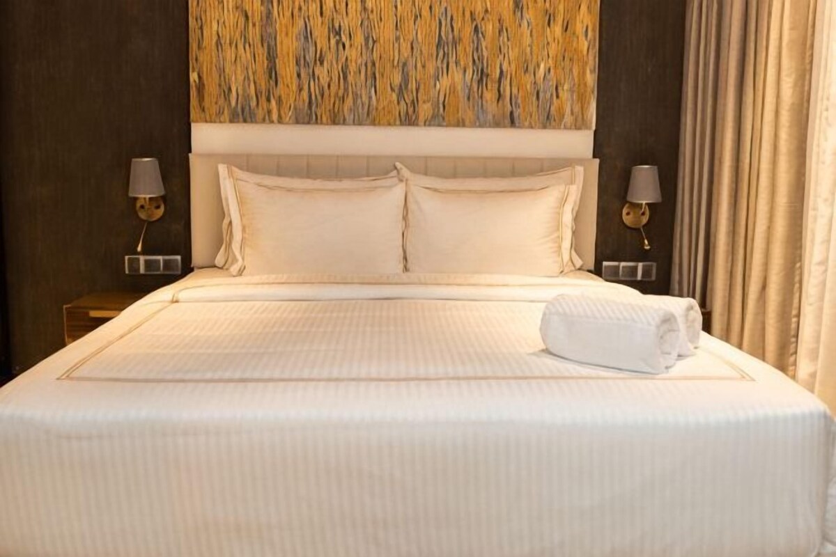 A neatly made bed with white linens, two bedside lamps, and a headboard with a patterned design.