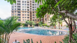 Une piscine entourée d’une terrasse en bois, avec un grand immeuble d’habitation en arrière-plan.