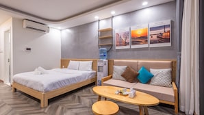 Une chambre d’hôtel moderne avec un lit, un canapé et une petite table. On y trouve un climatiseur, un distributeur d’eau et deux tableaux encadrés accrochés au mur.