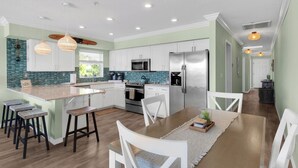 Una cocina moderna con gabinetes blancos, un refrigerador de acero inoxidable y una isla grande con taburetes de bar.