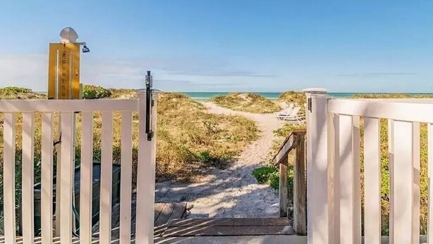 Un sendero bordeando la playa que desemboca en una extensión de arena, con una vista despejada del océano.