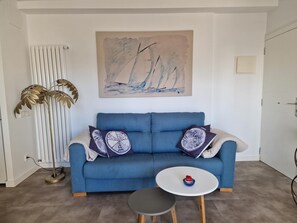 Un salon avec un canapé bleu, une table ronde blanche et un lampadaire.