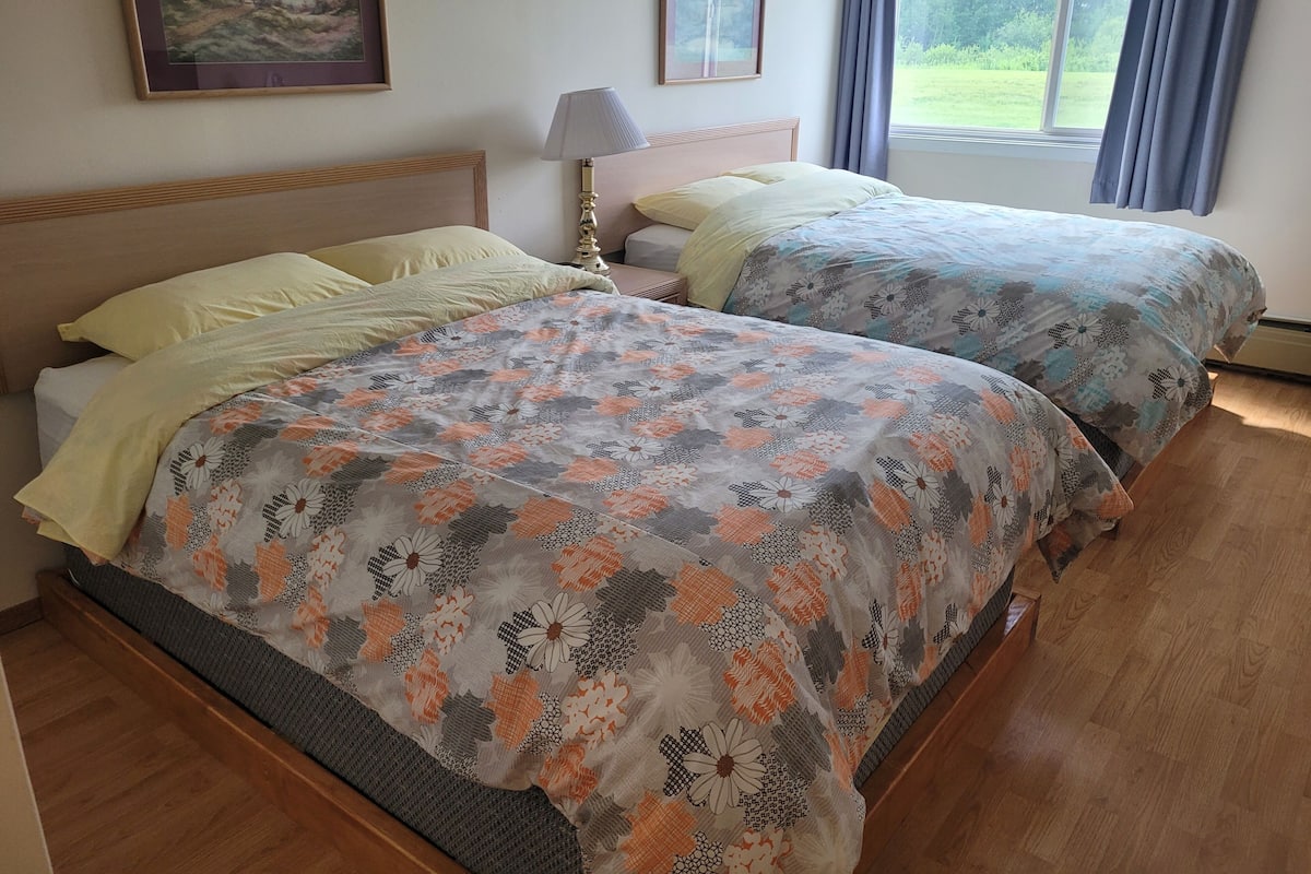 A room with two beds, a lamp, and a painting on the wall.