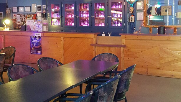 A bar with a wooden counter, multiple illuminated signs, and a seating area with tables and chairs. - Boyle Motor Inn (Boyle)