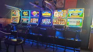 A row of slot machines in a dimly lit room with wooden chairs in the foreground. - Boyle Motor Inn (Boyle)