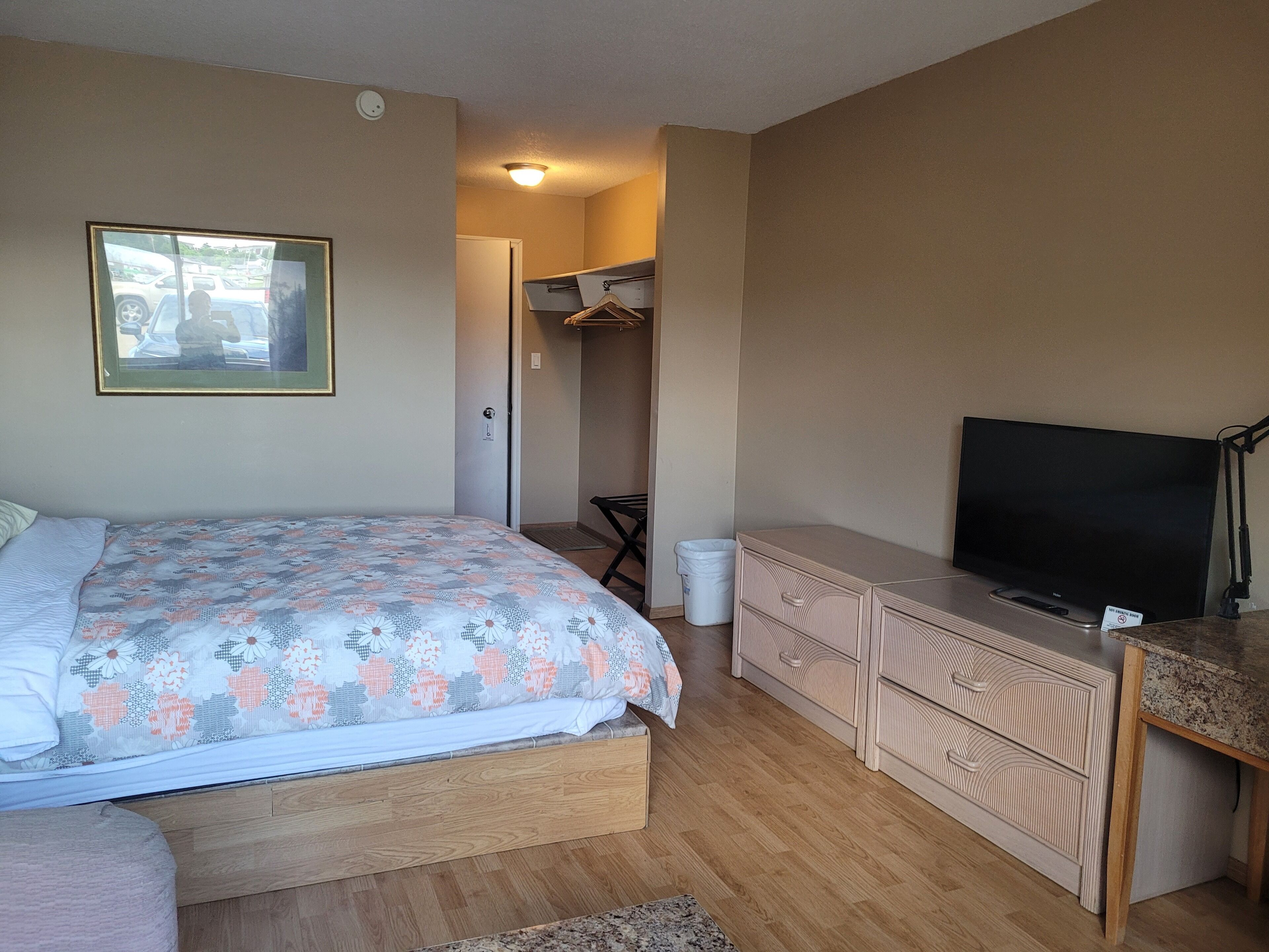 A bedroom with a bed, dresser, television, and a hallway leading to a bathroom.