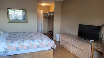 A bedroom with a bed, dresser, television, and a hallway leading to a bathroom.