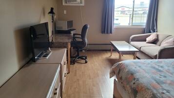 Habitación de hotel con cama, escritorio con computadora, silla, sofá y ventana con cortinas.