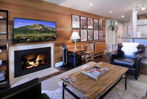 A living room with a fireplace, a television, a coffee table with magazines, and a fireplace mantel with framed pictures. - Ski in/Bike out, Updated, 2BD/2BA Emmons Condo, ski in/ski out (Crested Butte)