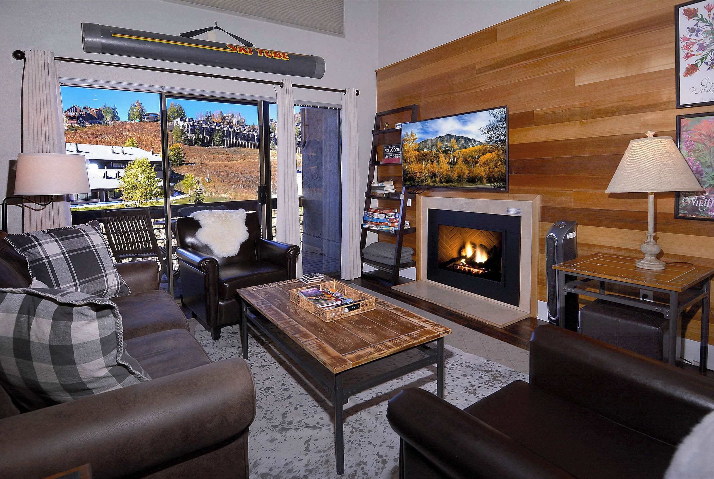 A living room with a fireplace, a television, and a view of a mountain landscape.