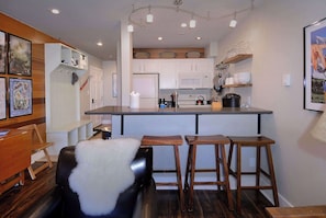 A modern kitchen with white cabinets, a central island with stools, a refrigerator, and a microwave. - Ski in/Bike out, Updated, 2BD/2BA Emmons Condo, ski in/ski out (Crested Butte)