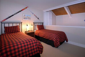 Un dormitorio con dos camas, una mesita de noche, una lámpara y una decoración con un bastón de esquí.