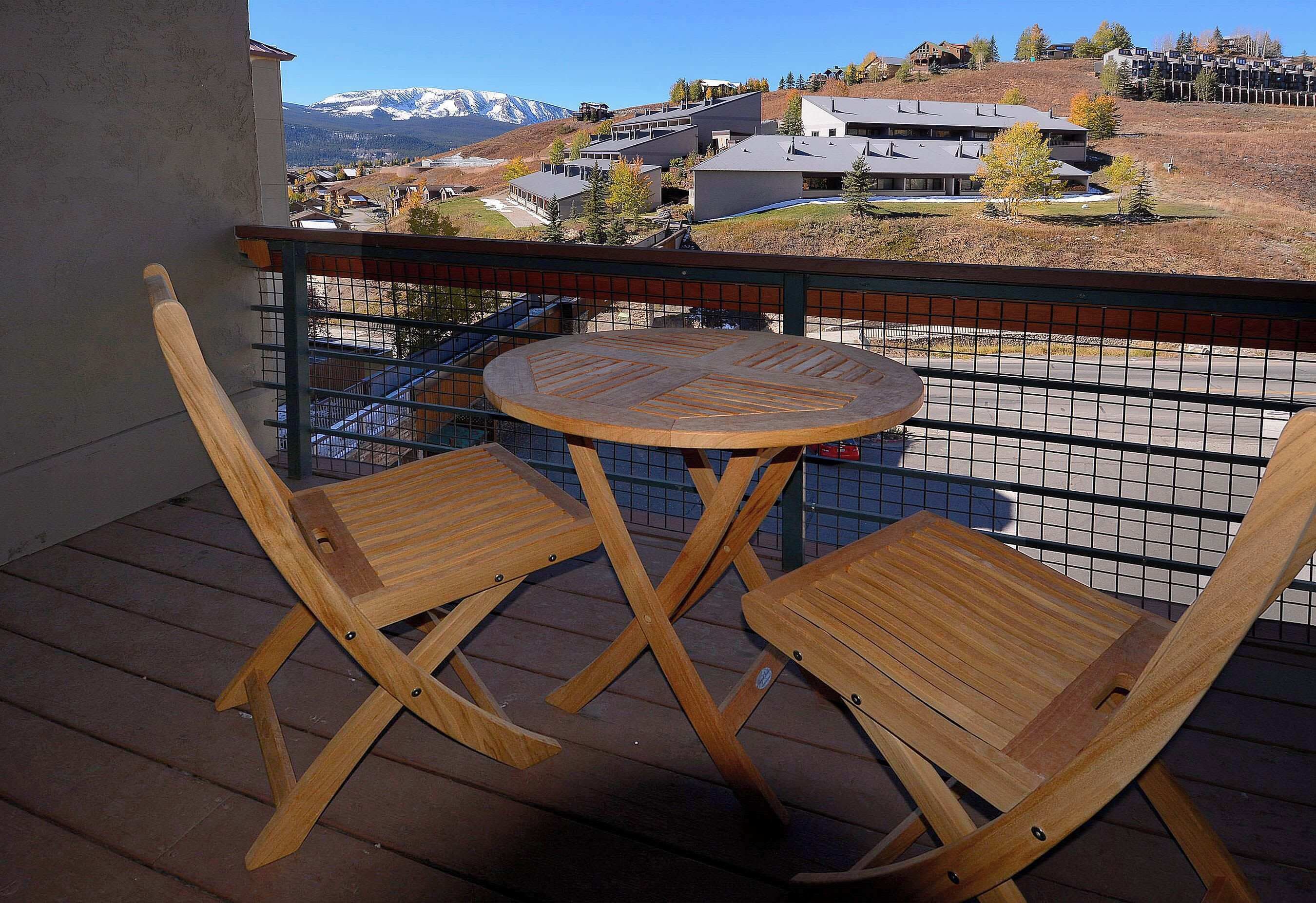Une terrasse en bois avec deux chaises et une table, d’où l’on a vue sur un quartier résidentiel avec des maisons et une montagne en arrière-plan.