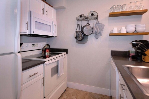 Una cocina con electrodomésticos blancos, estufa, horno, microondas y un colgador para ollas.