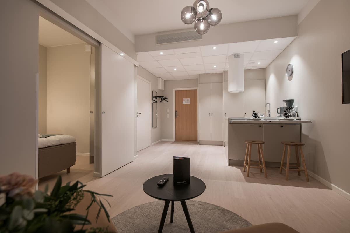 Una habitación de hotel moderna con kitchenette, una cama y una pequeña mesa con un control remoto.