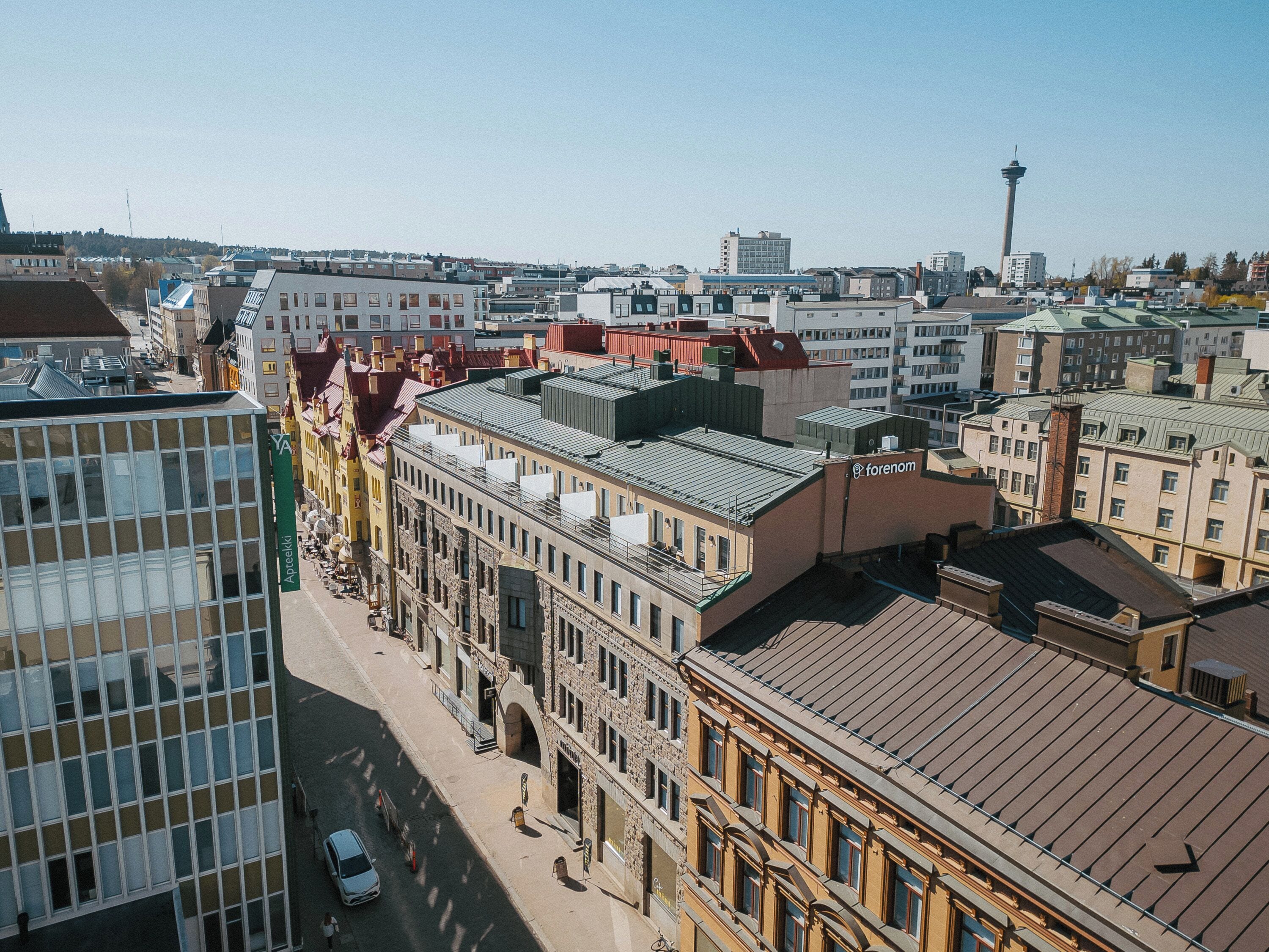 Korkea kerrostalo, jonka julkisivu on modernia lasia, sekä sen vieressä sijaitsevat vanhemmat rakennukset perinteisellä arkkitehtuurilla. Taustalla avautuu selkeä näkymä kaupungin siluettiin.