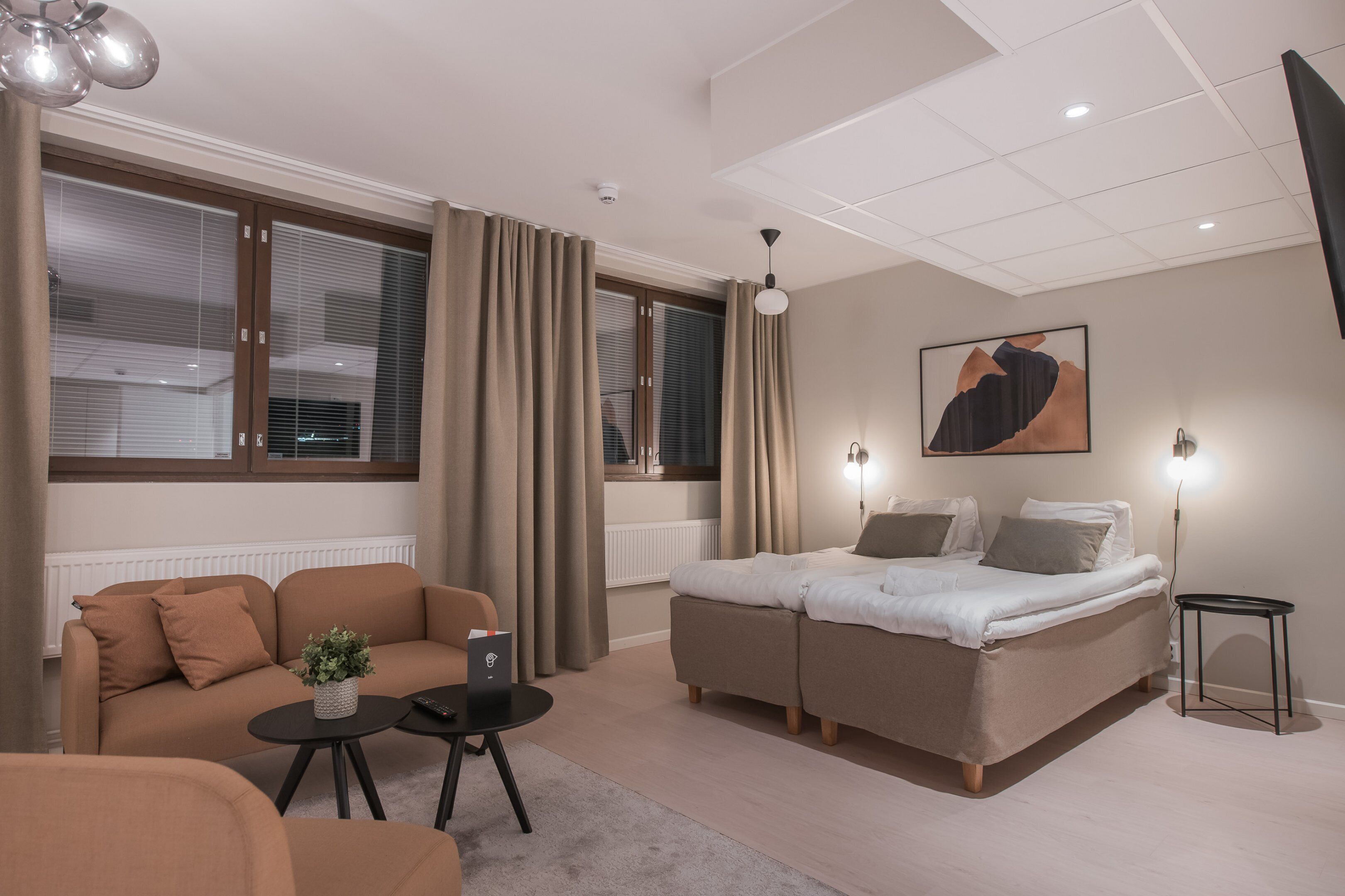 A modern hotel room with a sofa, a bed, a small table, and a lamp.