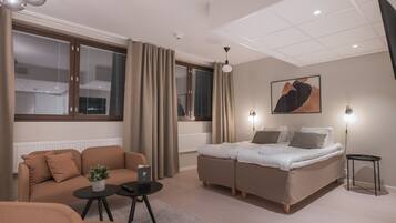 A modern hotel room with a sofa, a bed, a small table, and a lamp.