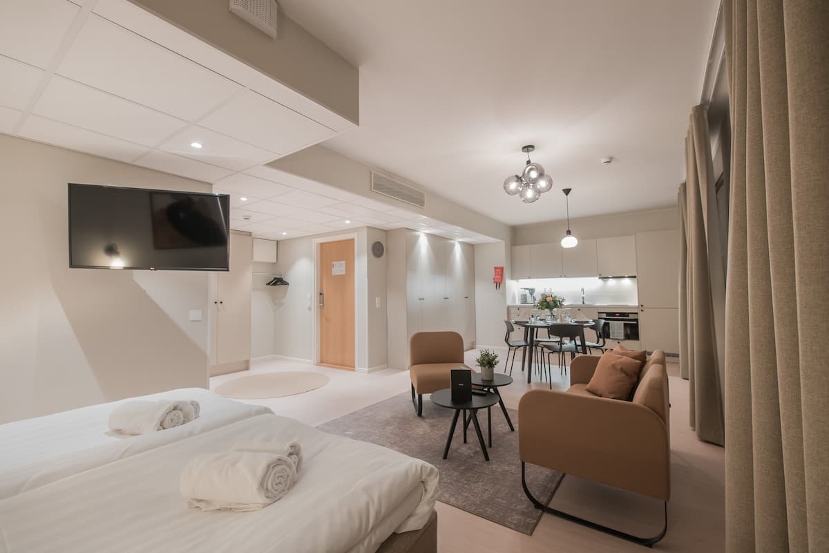 Una habitación de hotel moderna con una cama grande, un sofá, una mesita y un televisor montado en la pared.