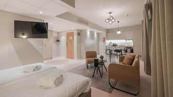 Una habitación de hotel moderna con una cama grande, un sofá, una mesita y un televisor montado en la pared.