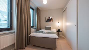 A bedroom with a bed, a bedside table, a lamp, a window with curtains, and a wall-mounted picture.