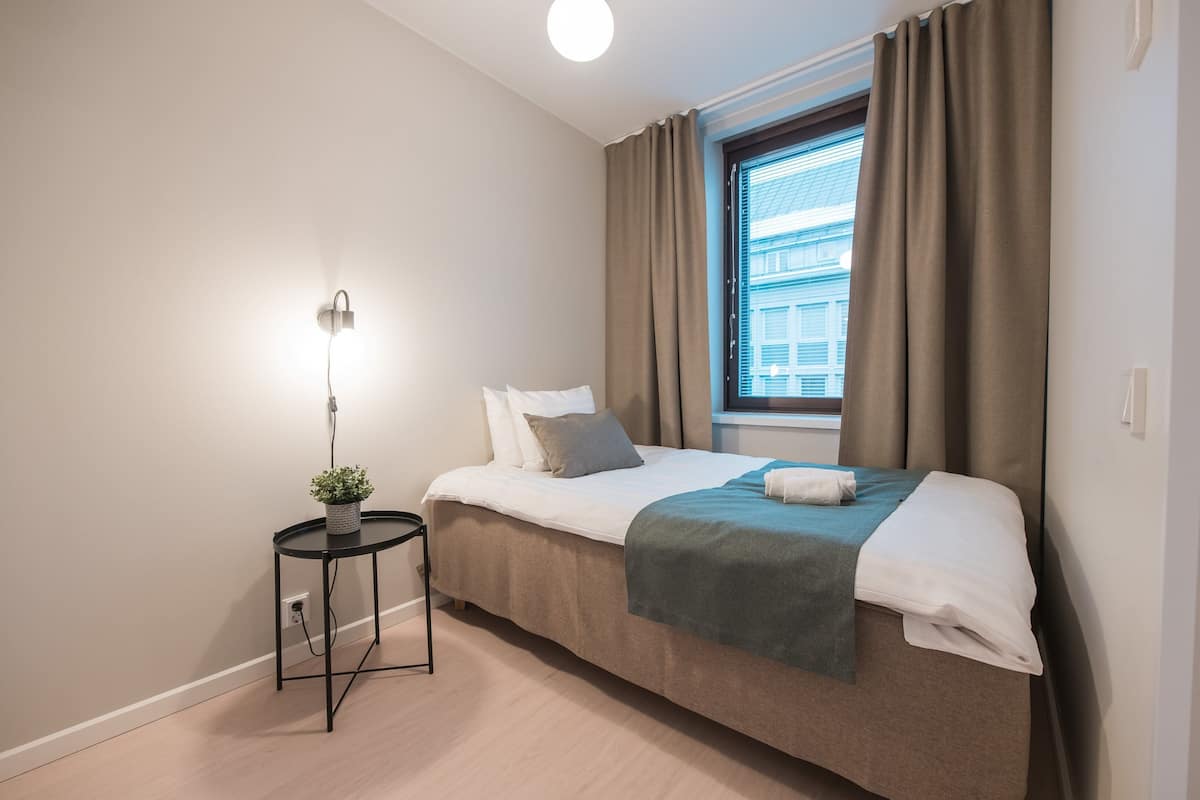 Una habitación de hotel moderna con una cama, una mesita de noche con una planta y una ventana con cortinas.