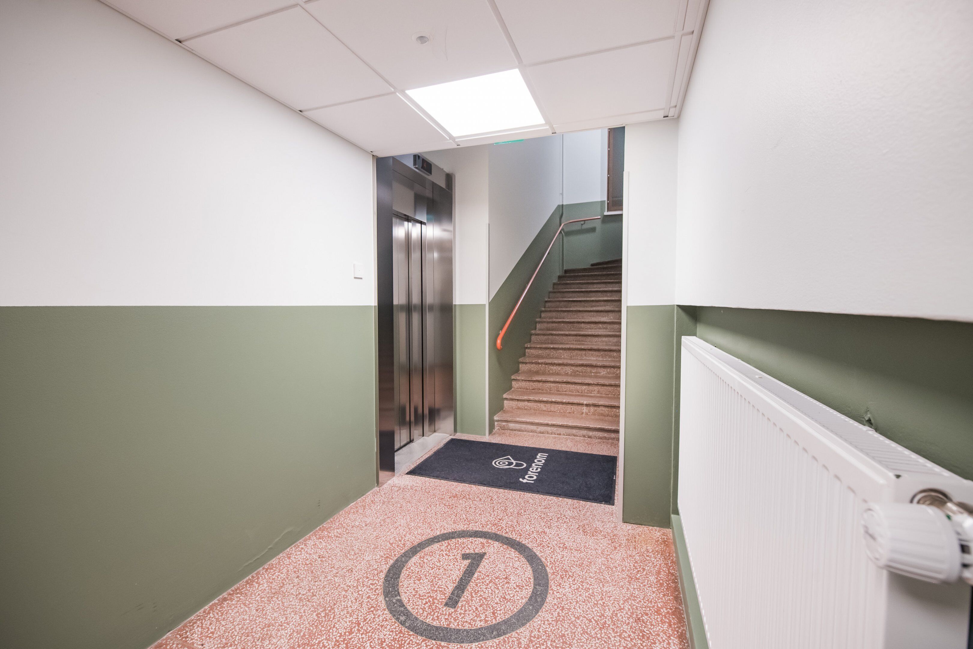 A hallway with a green wall, a white ceiling, and a staircase leading to an elevator.