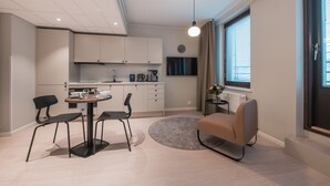 A modern kitchen with white cabinets, a dining area with a round table and chairs, a sofa, and a large window with blinds. - Forenom Aparthotel Tampere Kauppakatu (Tampere)