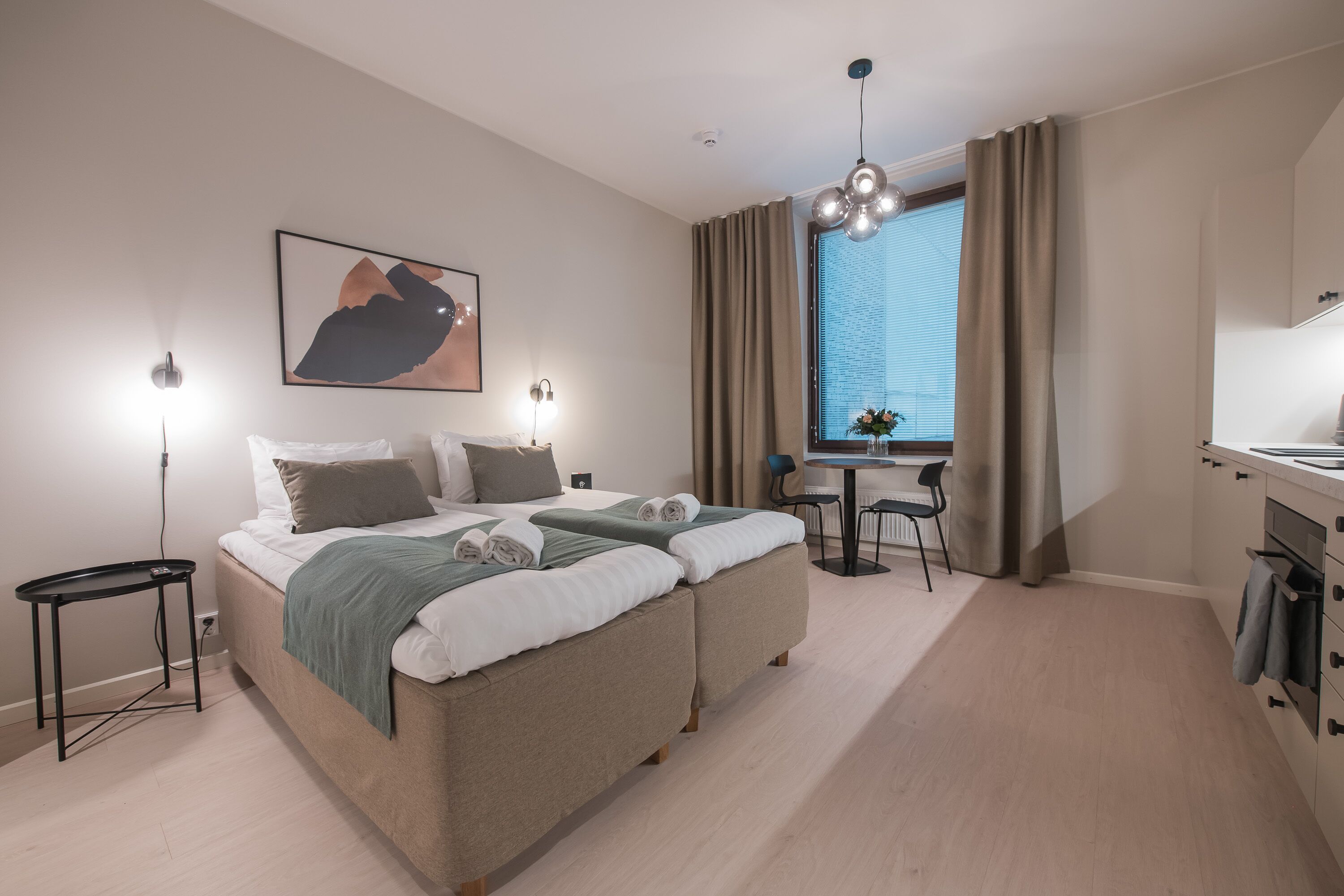 A modern hotel room with a bed, bedside tables, a desk, and a window with curtains.