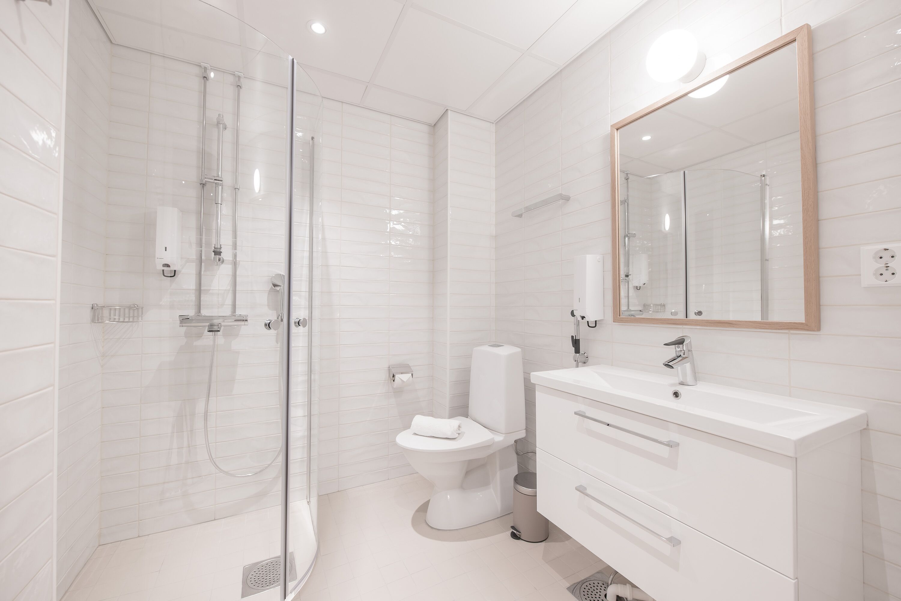 Een moderne badkamer met een douchecabine van glas, een wit toilet en een wastafel met lades.