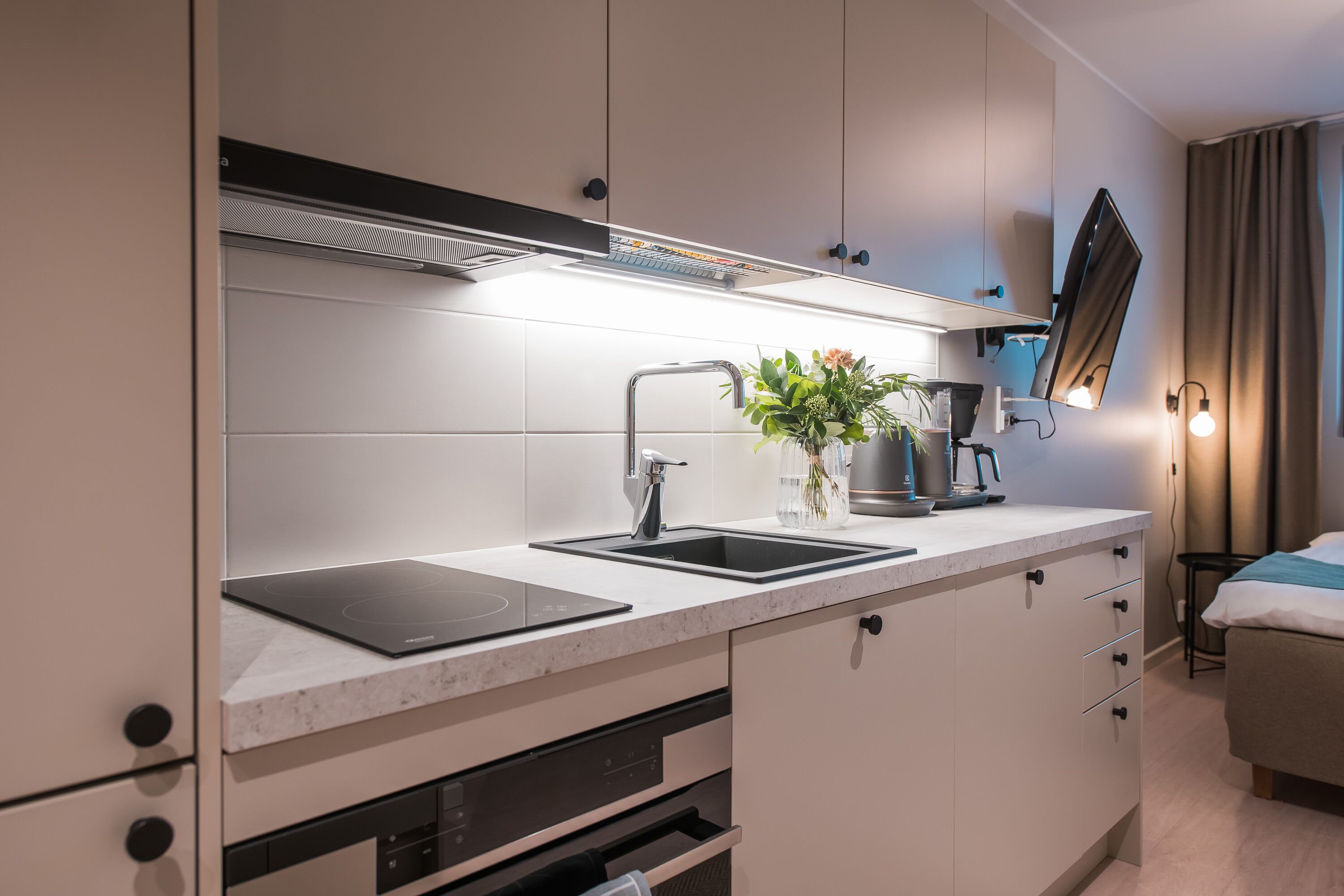 A modern kitchen with a built-in stove, sink, and a flat-screen TV mounted on the wall.