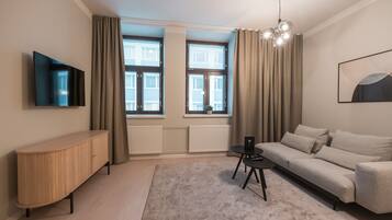 A modern living room with a sofa, a TV mounted on the wall, a small table, and a large window with curtains.