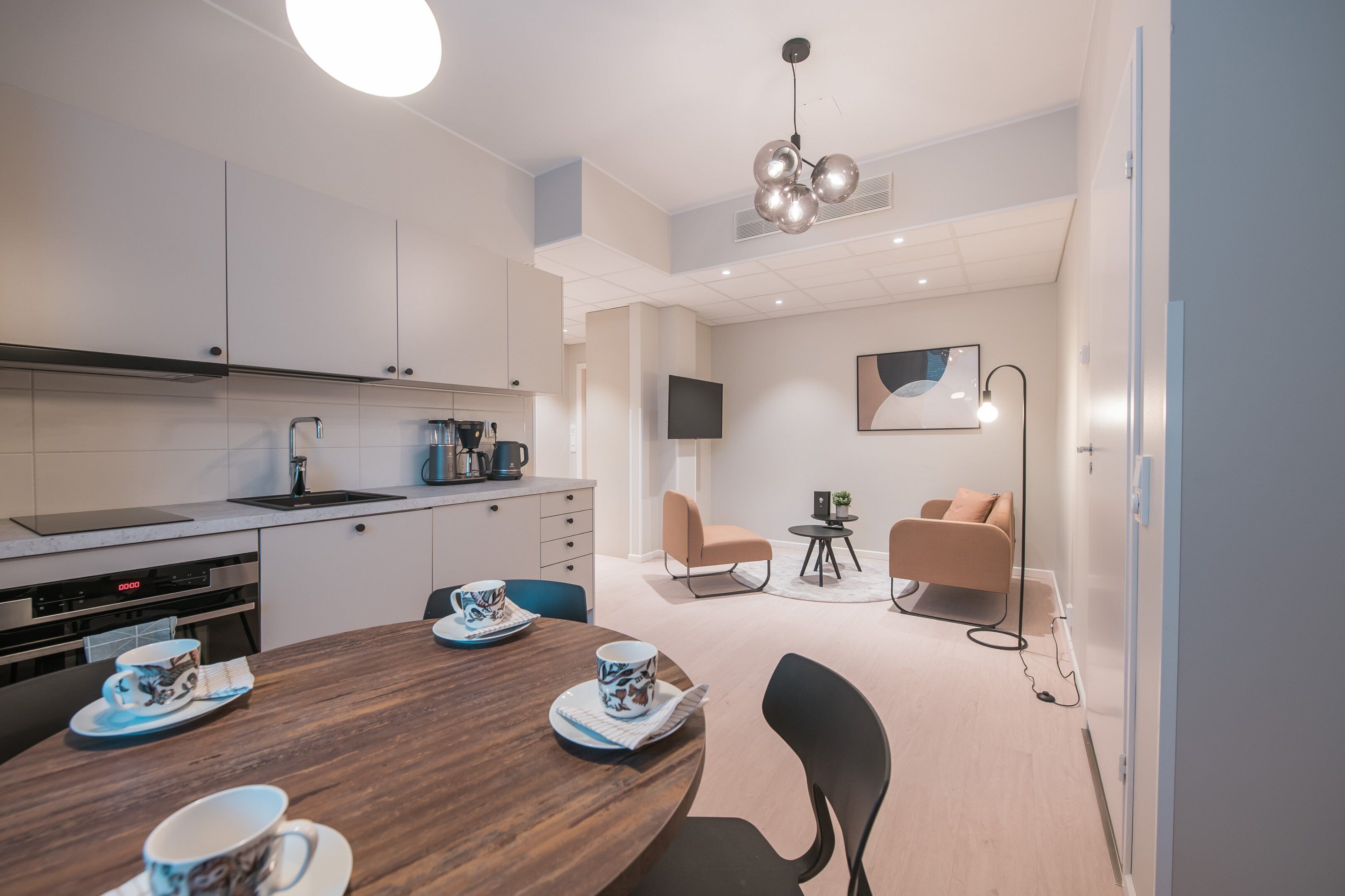 Een moderne keuken met een eethoek, inclusief een houten tafel met borden en kopjes, een koffieapparaat en een televisie aan de muur.