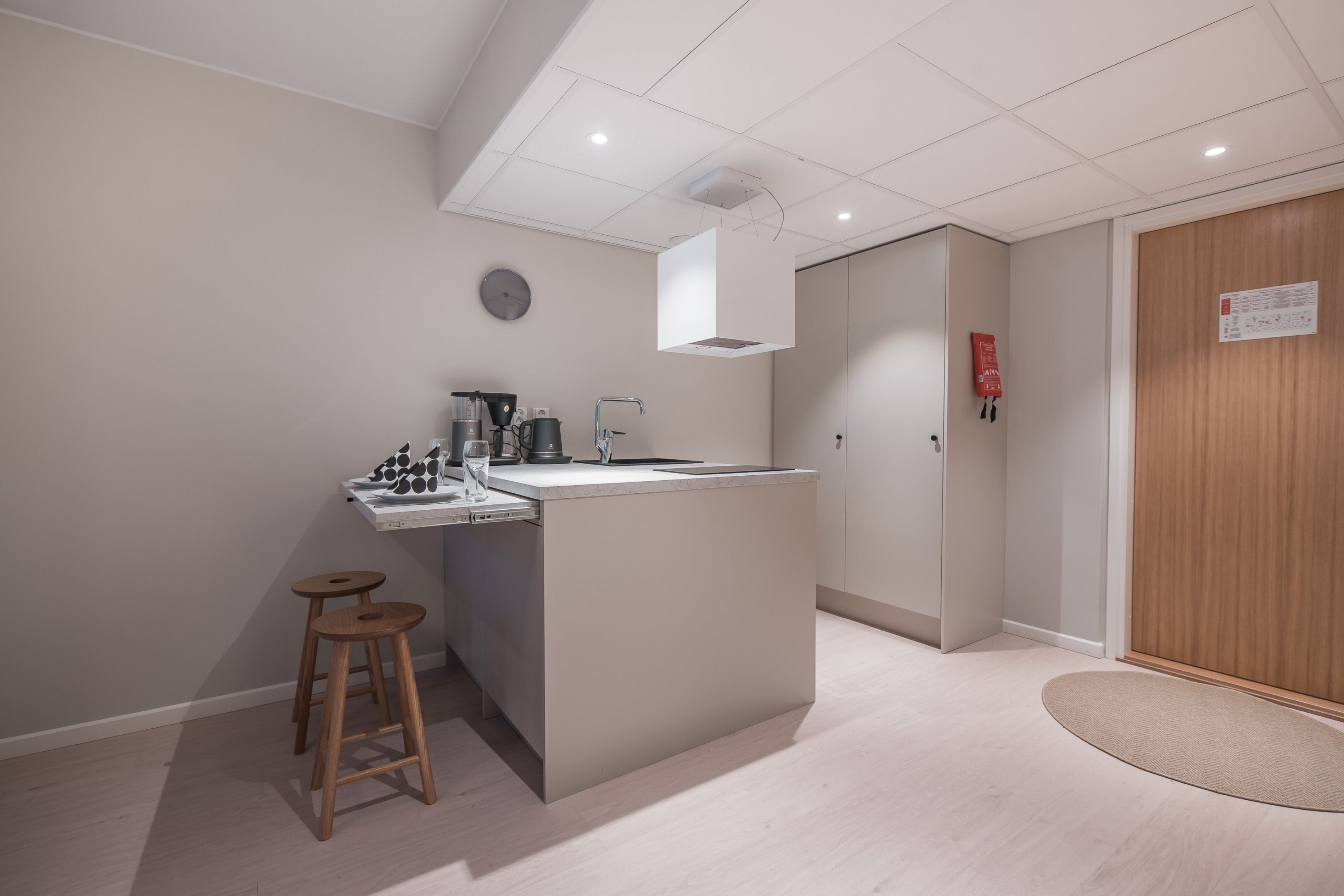 A modern kitchen with a central island, stools, and a clock on the wall.