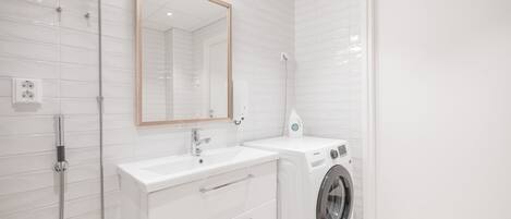 A modern bathroom with white tiles, a sink, a mirror, and a washing machine.