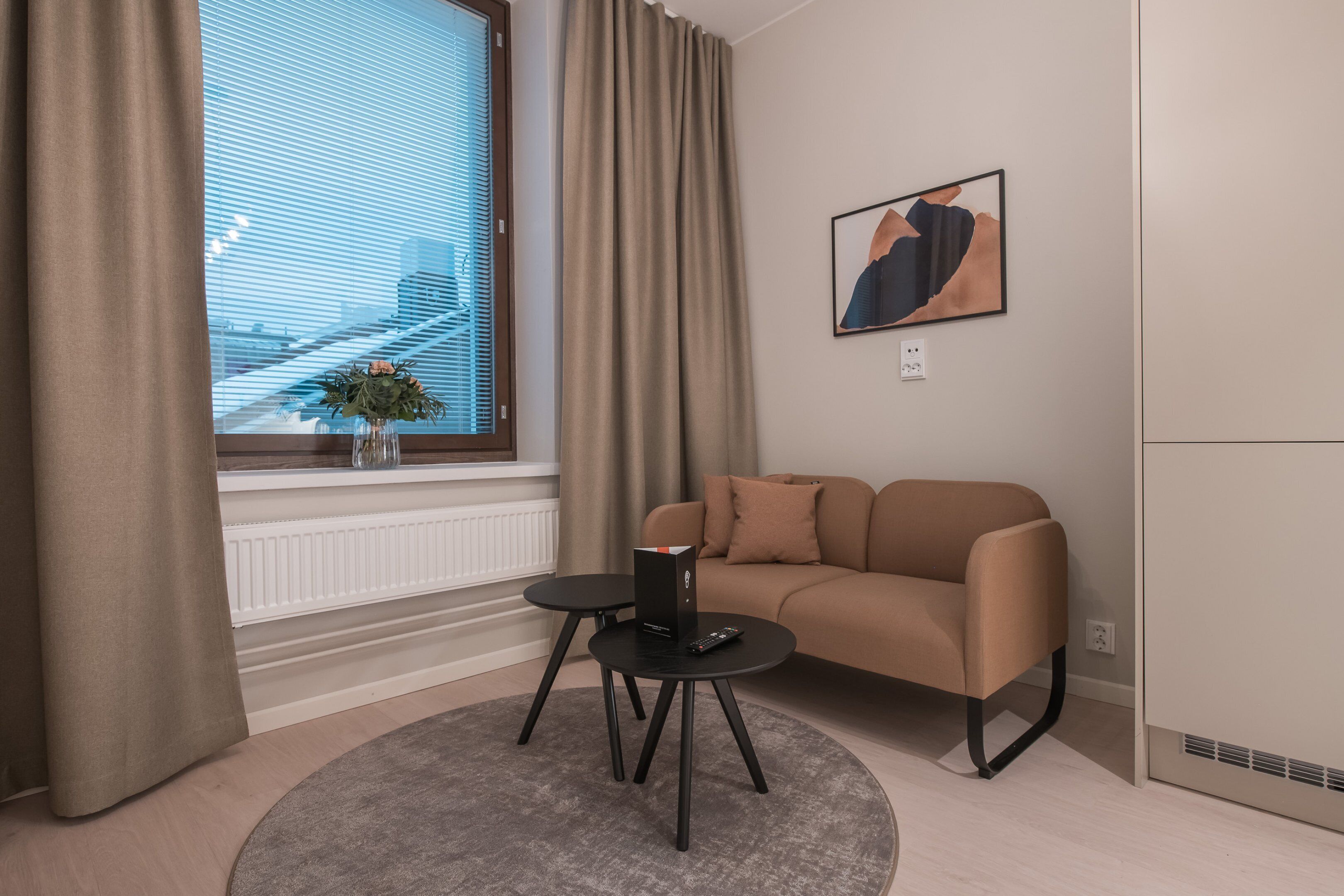 A modern living room with a beige sofa, a small round table, and a window with curtains.