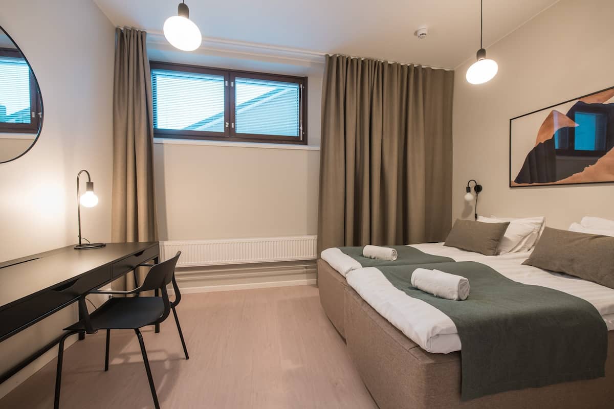 Una habitación de hotel moderna con cama, escritorio, silla y un ventanal con cortinas.