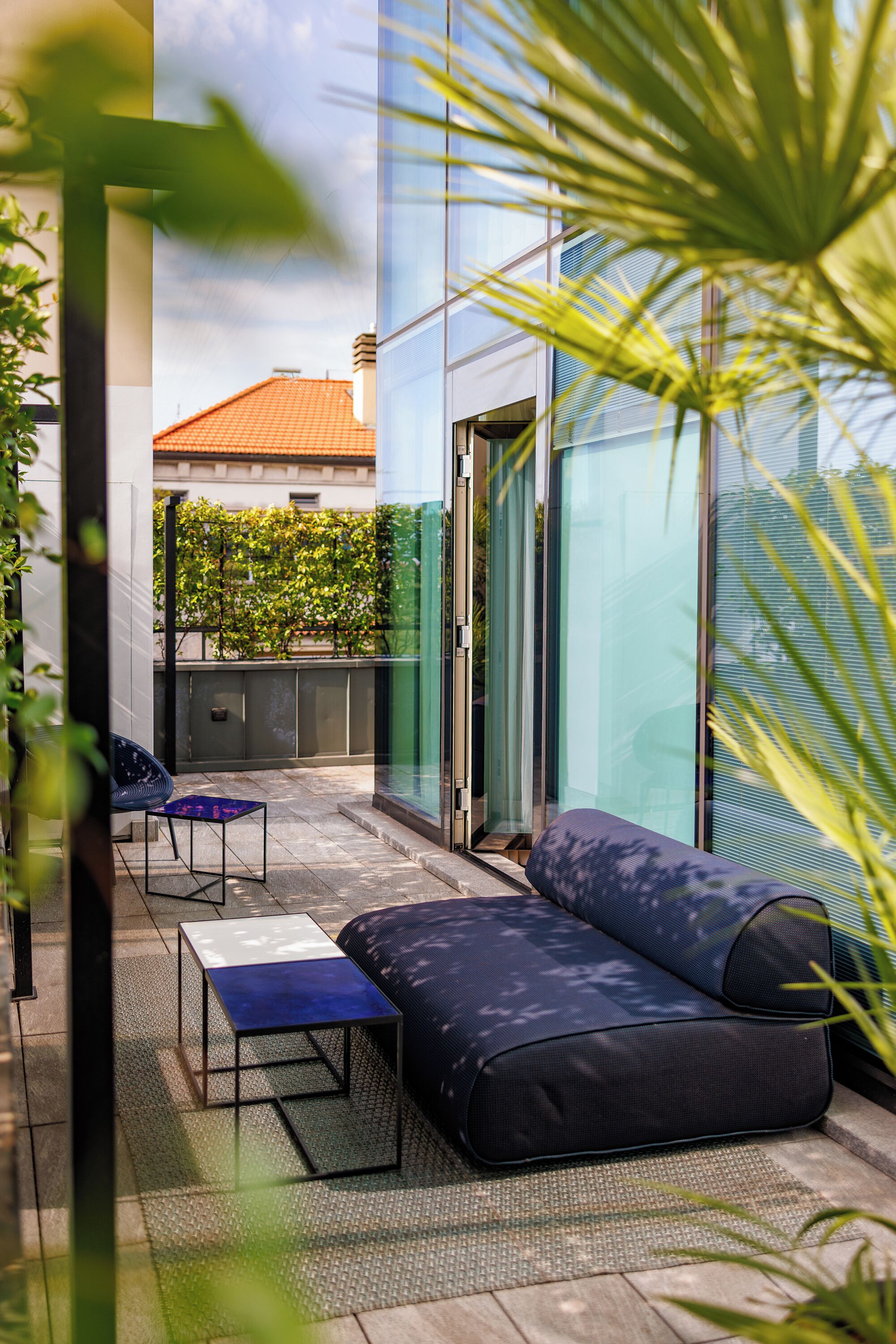 A modern outdoor seating area with a sofa and a small table, surrounded by glass walls and plants.