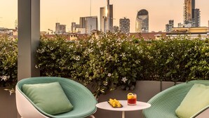 A rooftop terrace with two green cushioned chairs, a small table with a drink, and a city skyline view. - Casa Baglioni Milan - The Leading Hotels of the World (Milan)