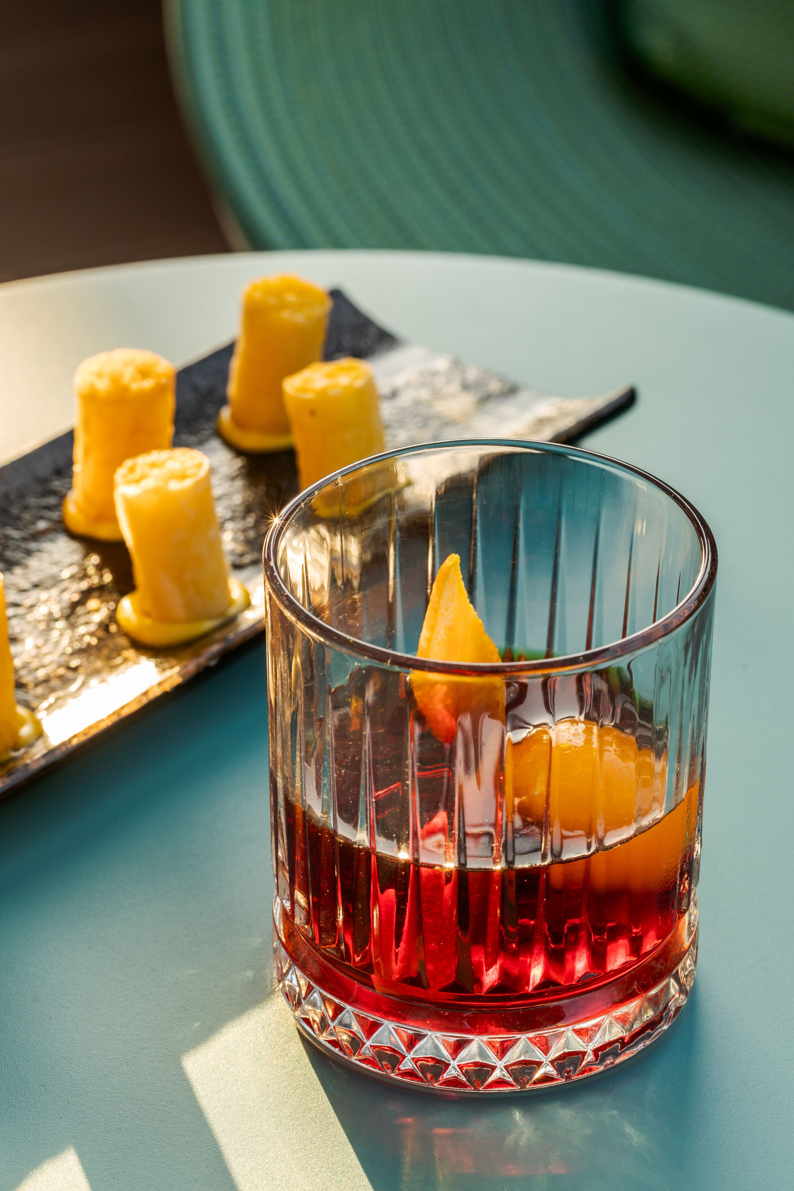 A glass with a red liquid and a yellow garnish on a blue table.